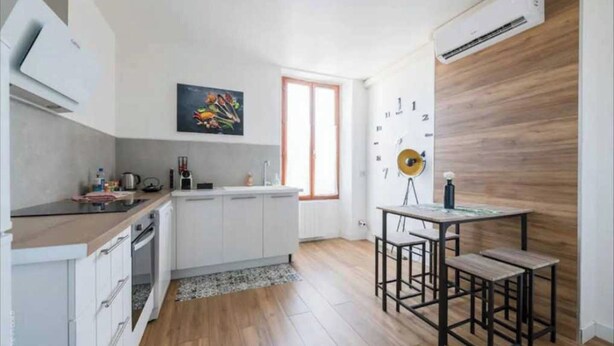 A compact kitchen with white cabinets, a wooden countertop, and a dining area with a small table and stools.