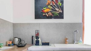 A modern kitchen with a white countertop, a kettle, a coffee maker, and a sink.