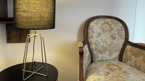 A room with a round table, a lamp with a textured shade, and a floral-patterned chair.