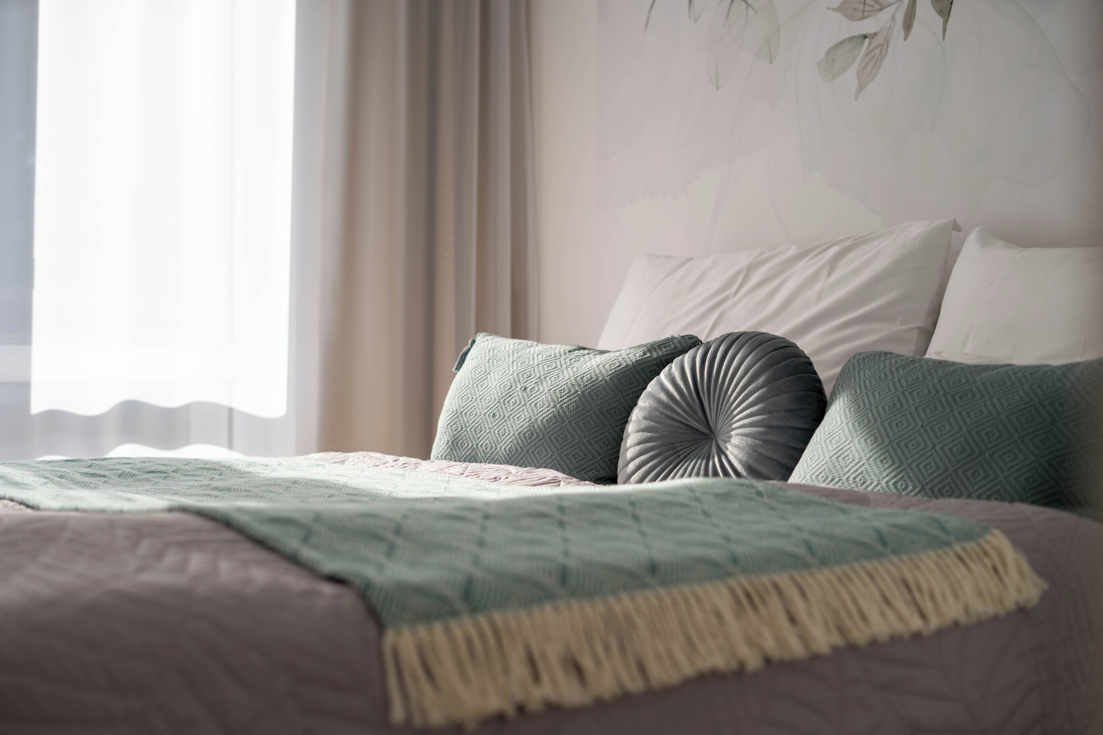 Un letto con una coperta e dei cuscini decorati, una finestra con tende e un muro con motivo a foglia.