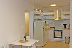 Una cocina compacta con electrodomésticos blancos, una mesa de comedor y un pequeño cubo de basura.