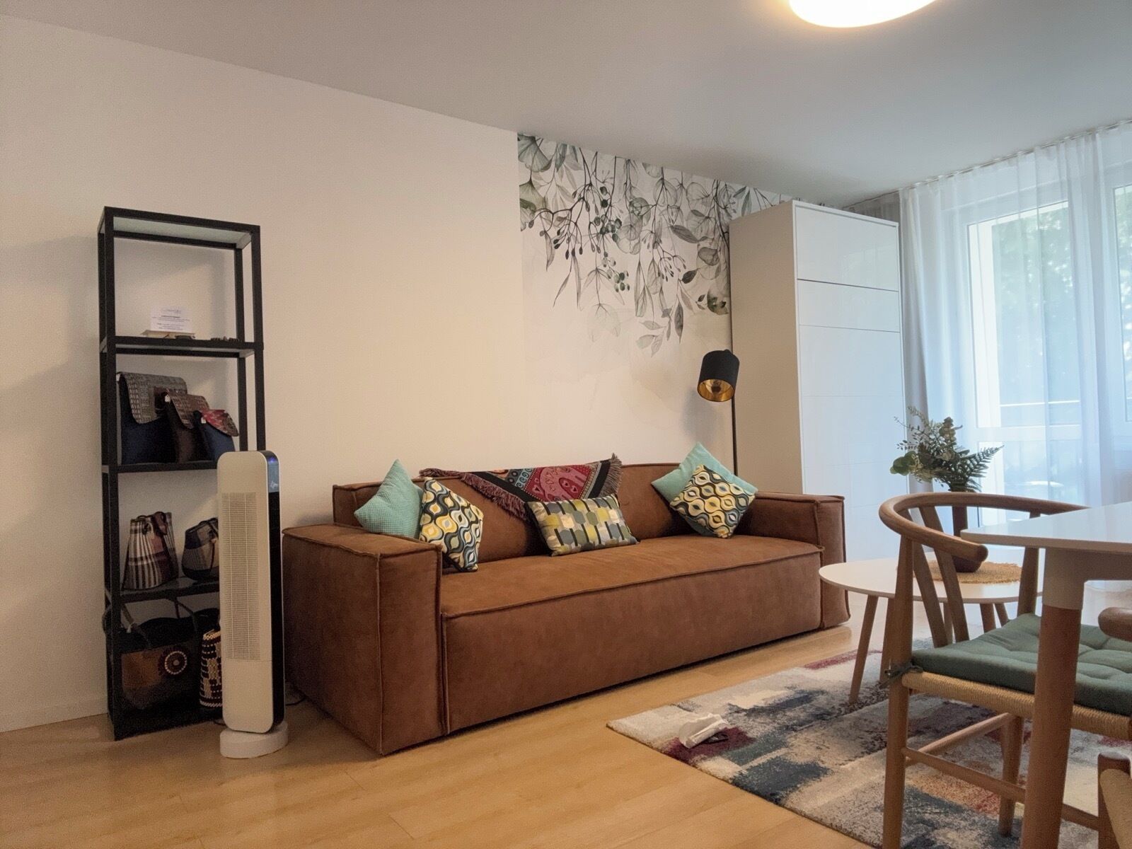 A cozy living area with a brown sofa, colorful cushions, a small table, and a floor lamp.