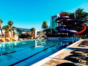 A swimming pool with clear blue water, surrounded by lounge chairs and a water slide.