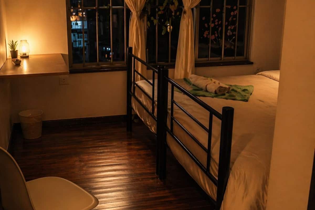 Une petite pièce avec un lit, une chaise, une fenêtre avec des rideaux et une petite lampe de chevet.