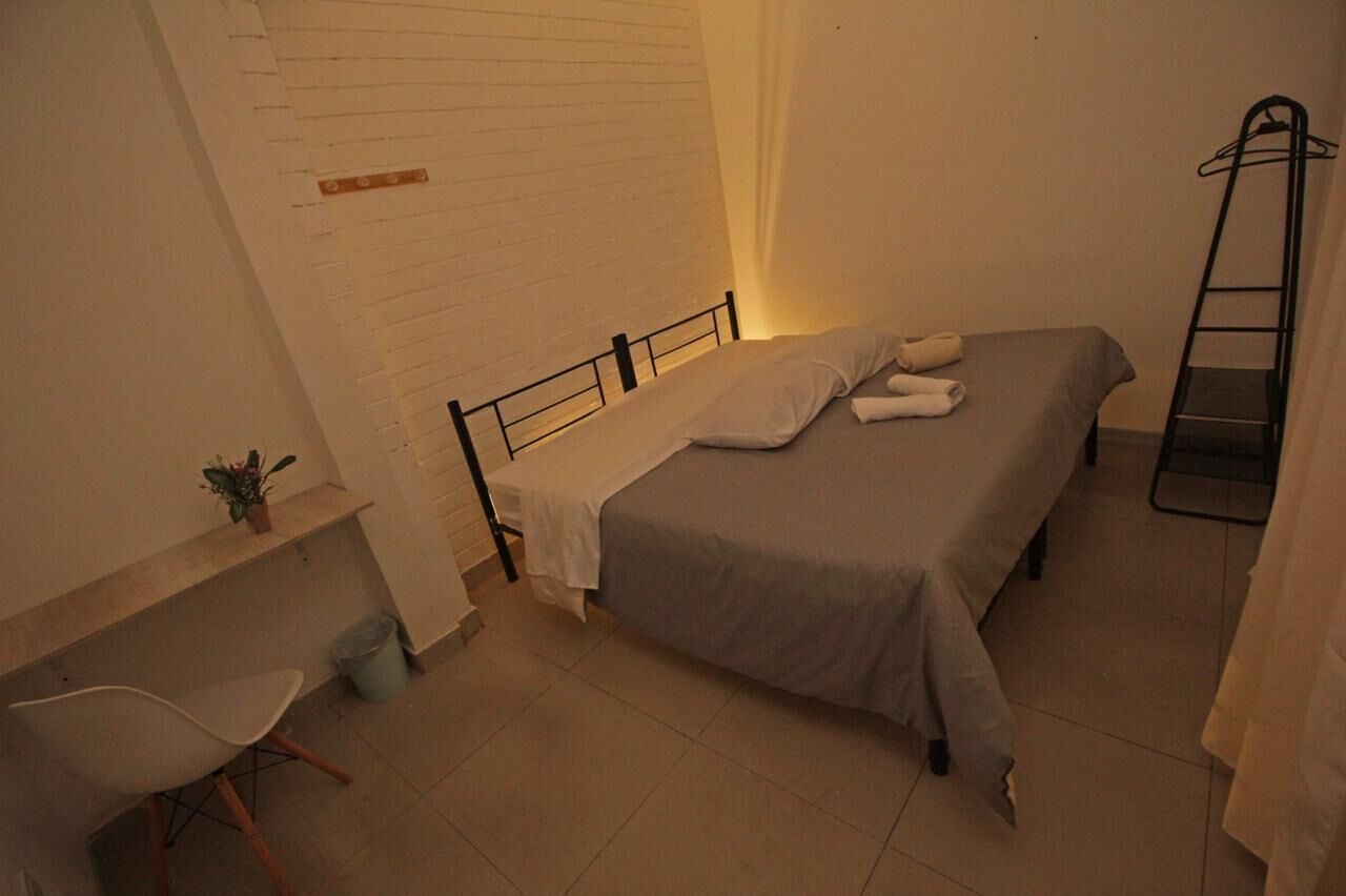 Um quarto pequeno e bem arrumado com uma cama de solteiro, uma cadeira e uma escrivaninha.