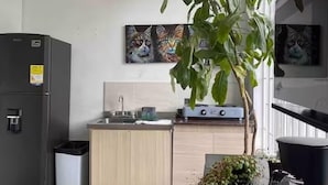 A compact kitchen with a refrigerator, sink, and stove. There is a potted plant and a vacuum cleaner on the floor. - Hotel El Encanto (Bogotá)