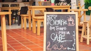 A cozy cafe with wooden tables and chairs, a chalkboard sign, and a green wall with plants. - Hotel El Encanto (Bogotá)
