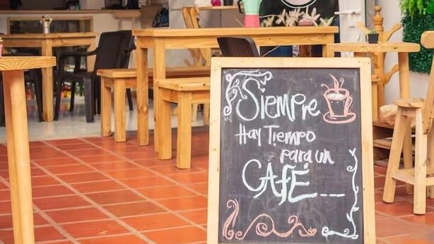 A cozy cafe with wooden tables and chairs, a chalkboard sign, and a green wall with plants. - Hotel El Encanto (Bogotá)