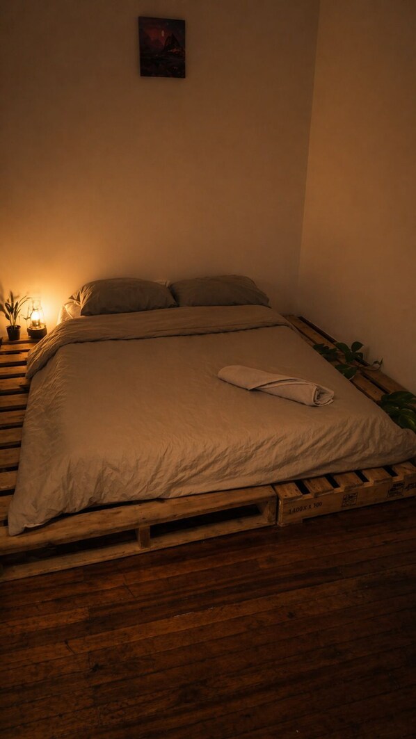 A bed with a blanket and pillows, a small table with a lamp, and a plant on the side. - Hotel El Encanto (Bogotá)