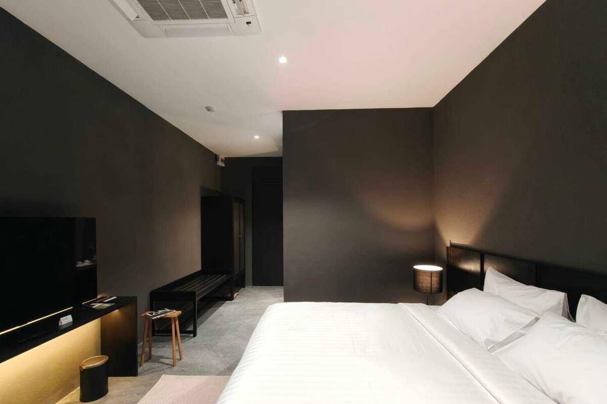 A modern hotel room with a large bed, a flat-screen TV, a small seating area, and a bedside table.