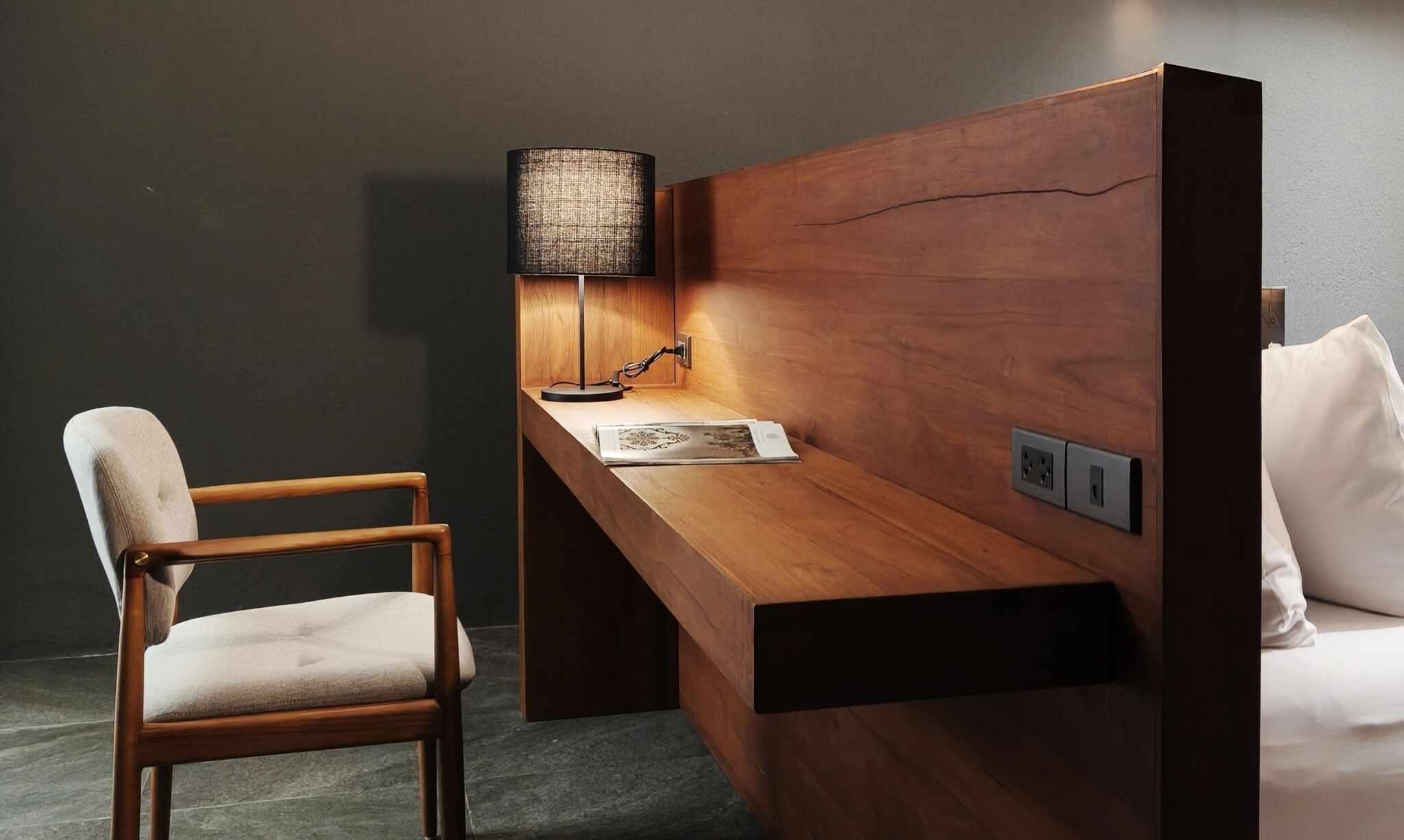 A modern room with a wooden desk, a chair, a lamp, and a bed.
