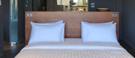 A double bed with a wooden headboard, a large mirror, and a view of a bathroom.