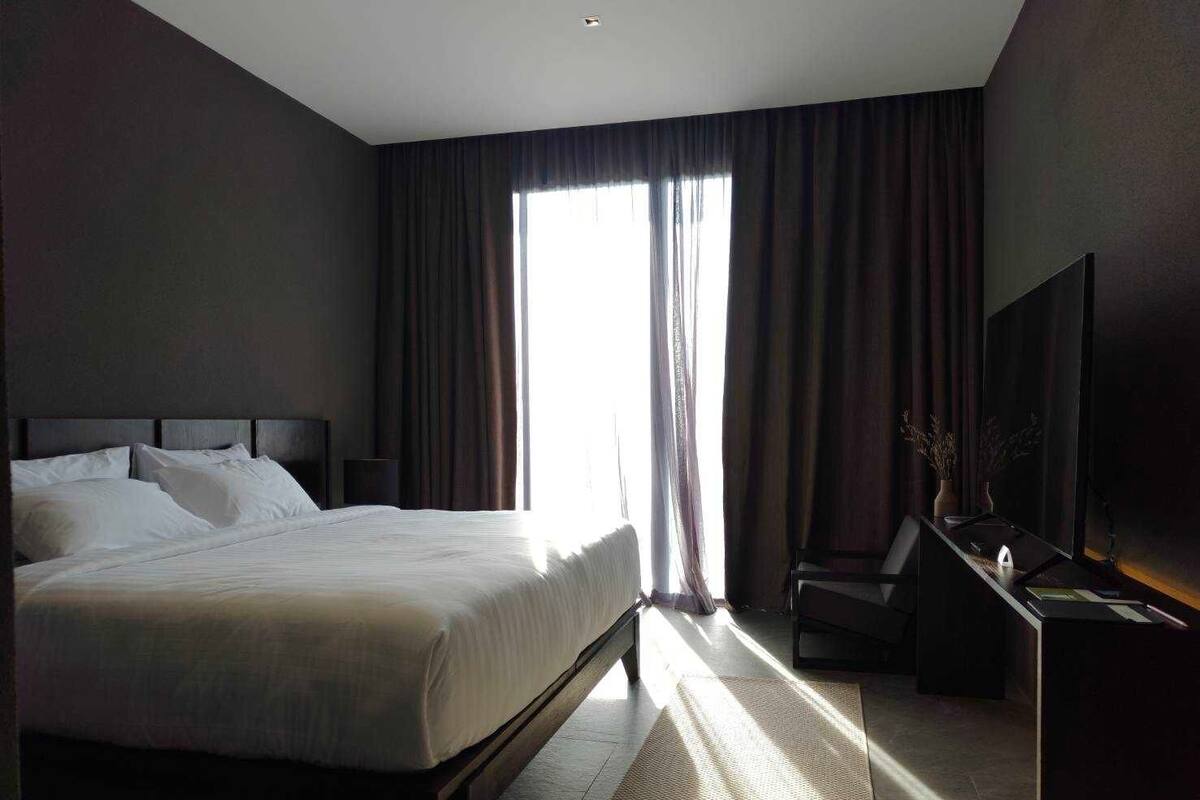 A modern hotel room with a large bed, a desk with a lamp, and a television.
