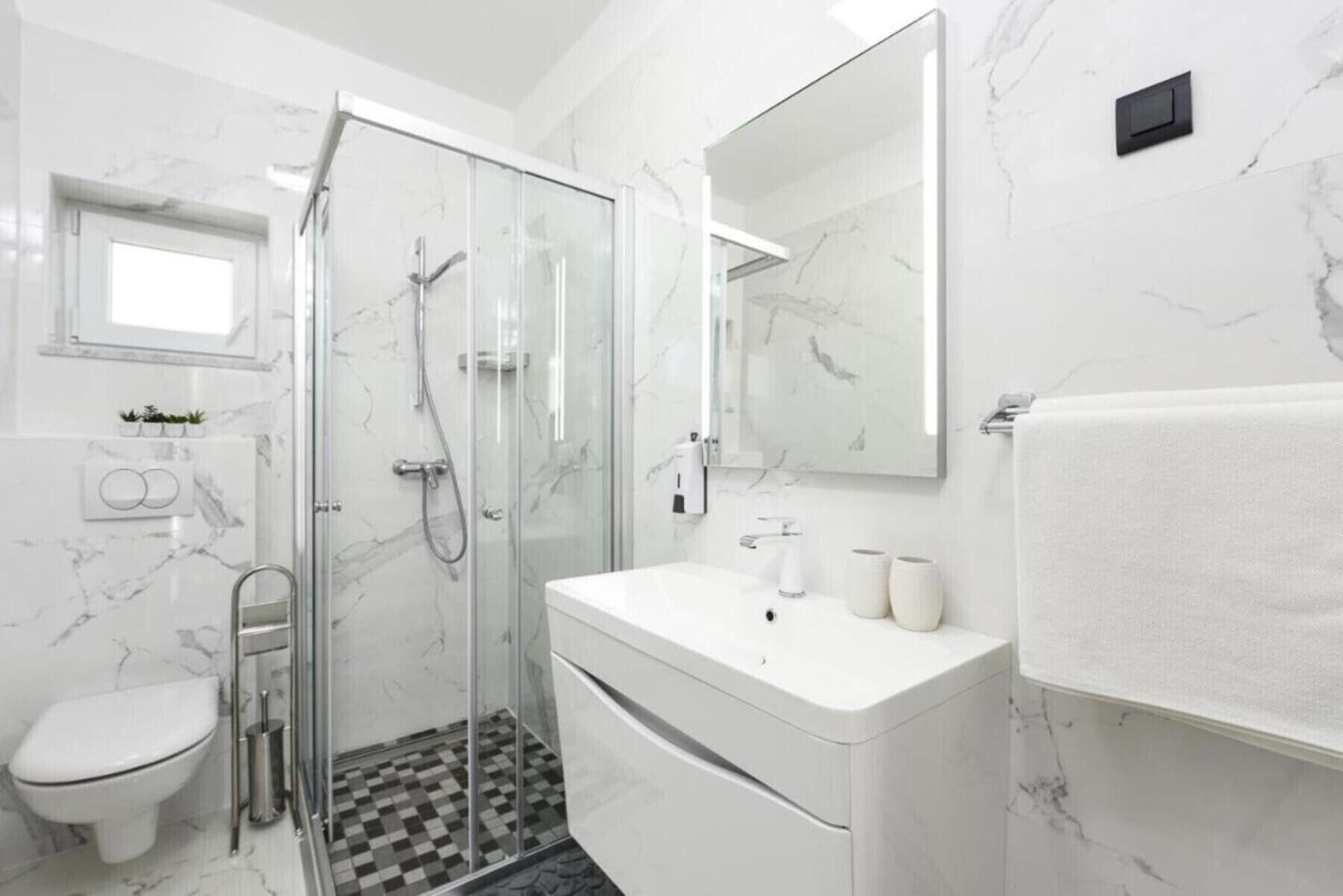 Un baño moderno con cabina de ducha de vidrio, un lavamanos blanco y suelo de baldosas de mármol.