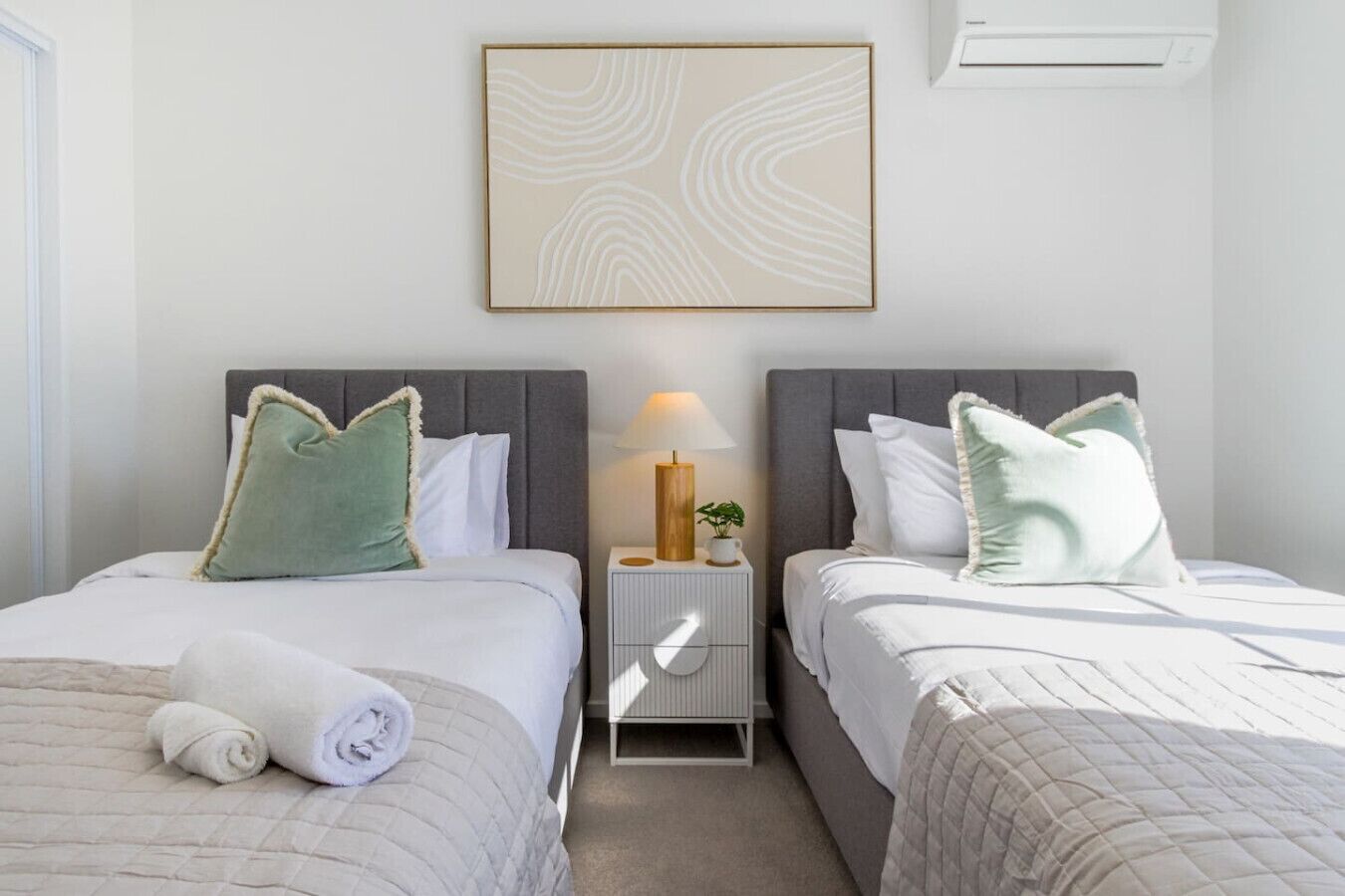 Ein Hotelzimmer mit zwei Betten, einem Nachttisch mit Lampe und einer Wand-Klimaanlage.