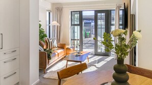 A modern living room with a sofa, coffee table, and a dining area with a vase of flowers.