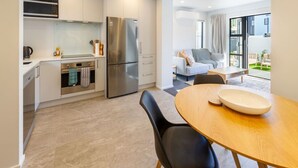 Una cocina moderna con electrodomésticos de acero inoxidable, un comedor con mesa redonda y sillas negras, y una sala de estar con sofá y vistas al exterior.
