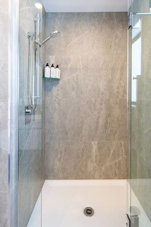 A modern shower with glass doors, a white bathtub, and a marble wall.