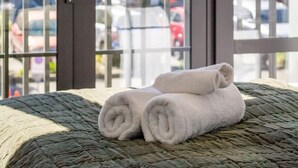 A bed with rolled towels and a view of parked cars through a glass door.