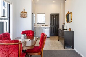 A dining area with a wooden table and red upholstered chairs, a kitchen with white cabinets, and a dark wooden cabinet with a mirror.