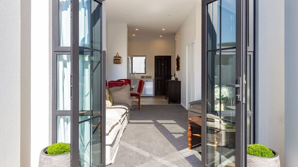 An open glass door leading to a living area with a sofa, a dining table, and a kitchen in the background.