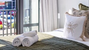 A hotel room with a bed, a window with a view of parked cars, and a balcony.