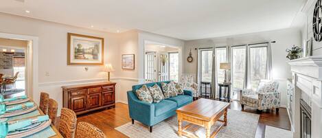 A spacious living room with a blue sofa, wooden coffee table, wicker chairs, and a dining area with a table set for four.
