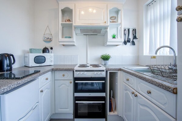 A compact kitchen with white cabinetry, a built-in oven, a microwave, and a sink with a faucet.