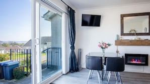 A balcony with a sliding glass door, a small table with two chairs, a flat-screen TV mounted on the wall, and a fireplace.