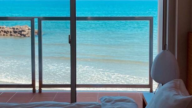 Ein Schlafzimmer mit großem Fenster mit Blick auf einen Strand.
