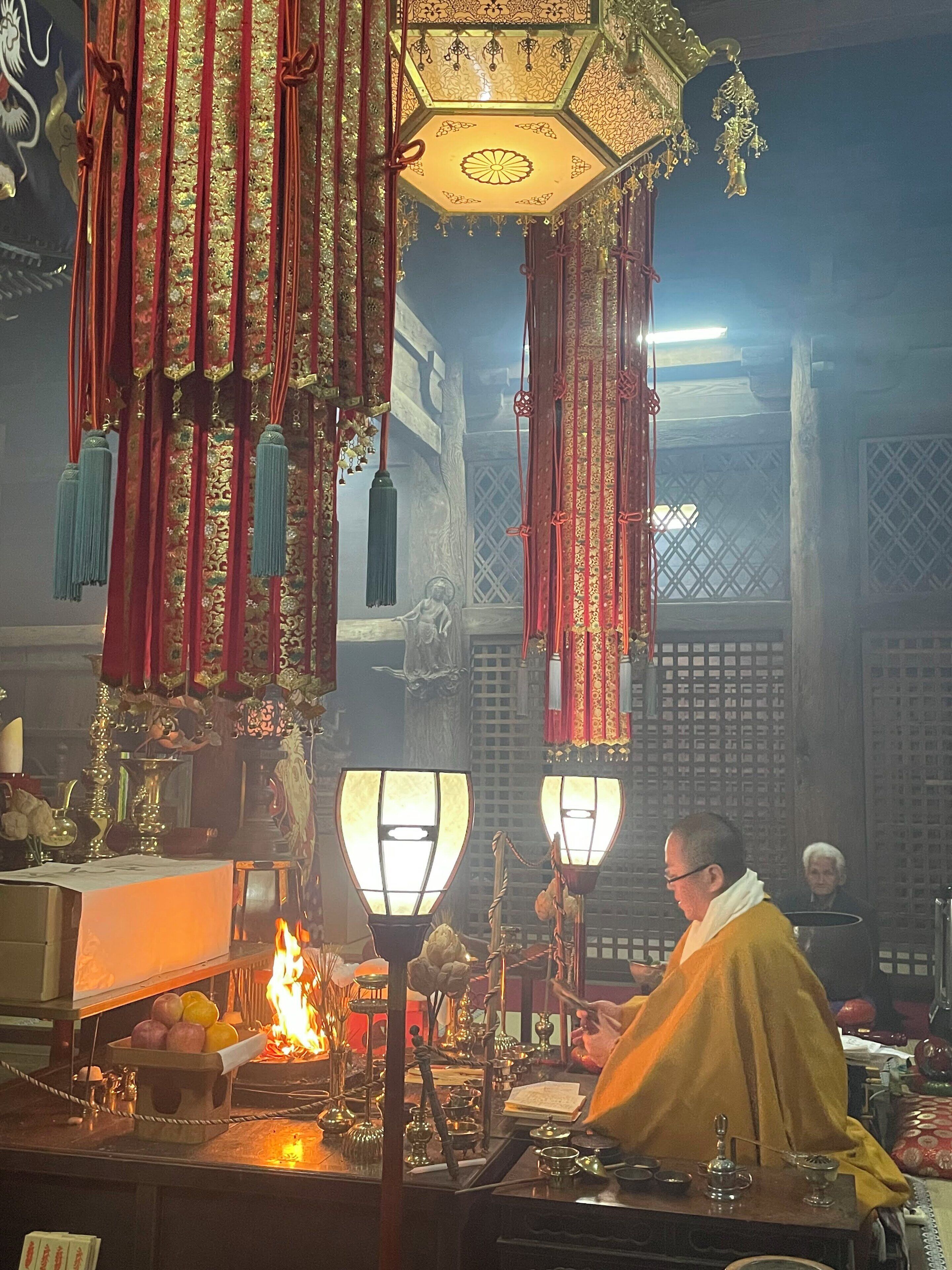 Interior de un templo tradicional con decoraciones ricamente ornamentadas, una figura central vestida de amarillo y objetos rituales.
