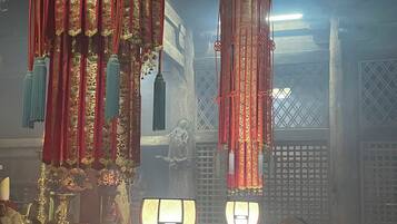 Interior de un templo tradicional con decoraciones ricamente ornamentadas, una figura central vestida de amarillo y objetos rituales.