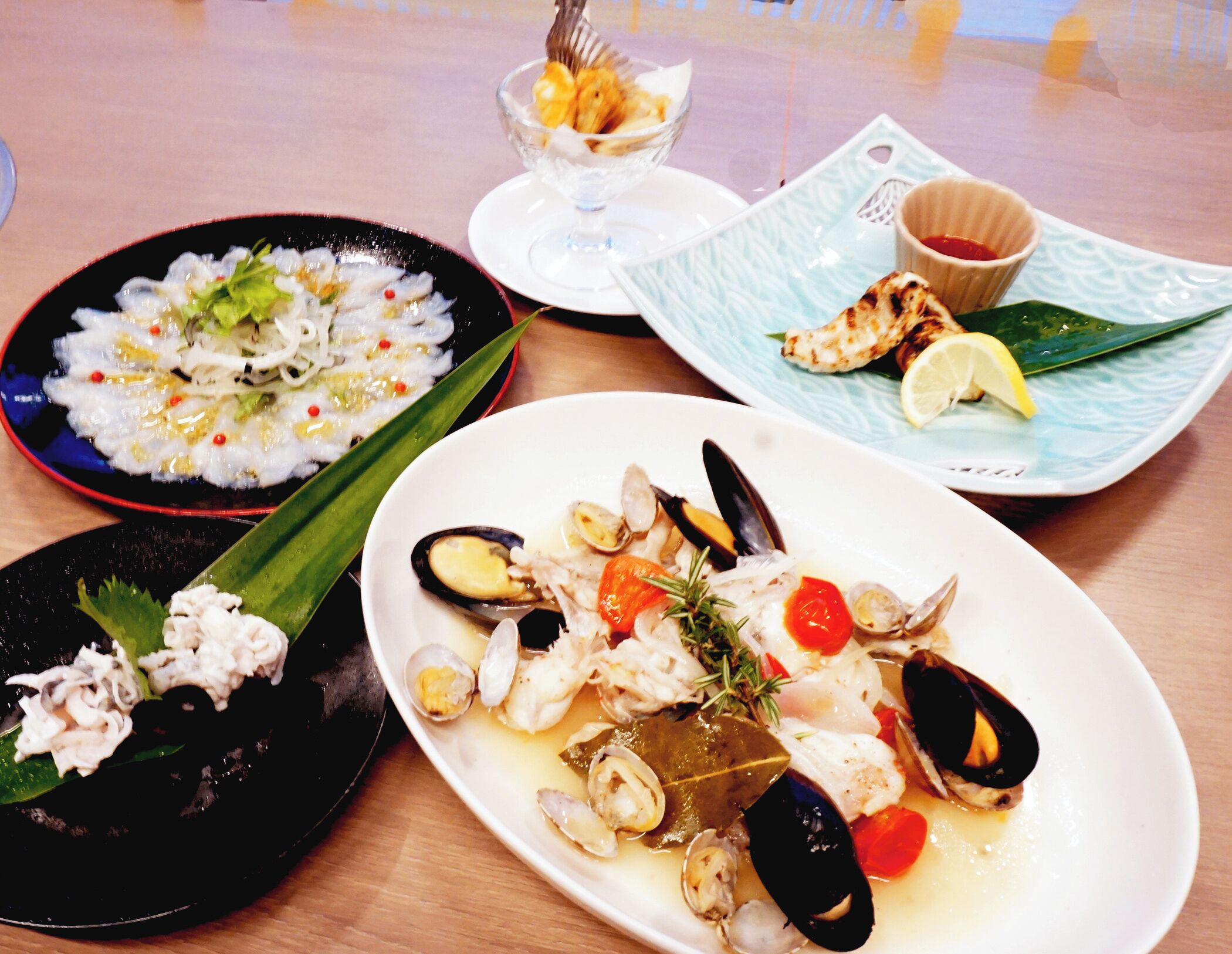 A table with three plates of seafood dishes, a small bowl of fruit, and a cup of sauce.