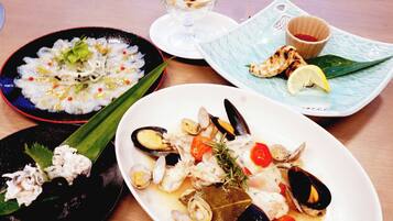 A table with three plates of seafood dishes, a small bowl of fruit, and a cup of sauce.