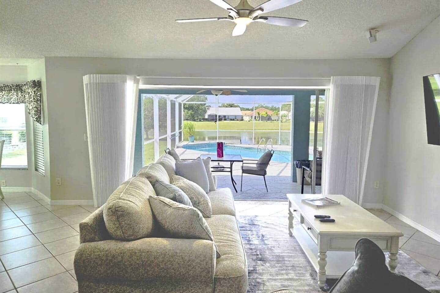 A spacious living room with a large sofa, a dining table, and a view of a swimming pool.