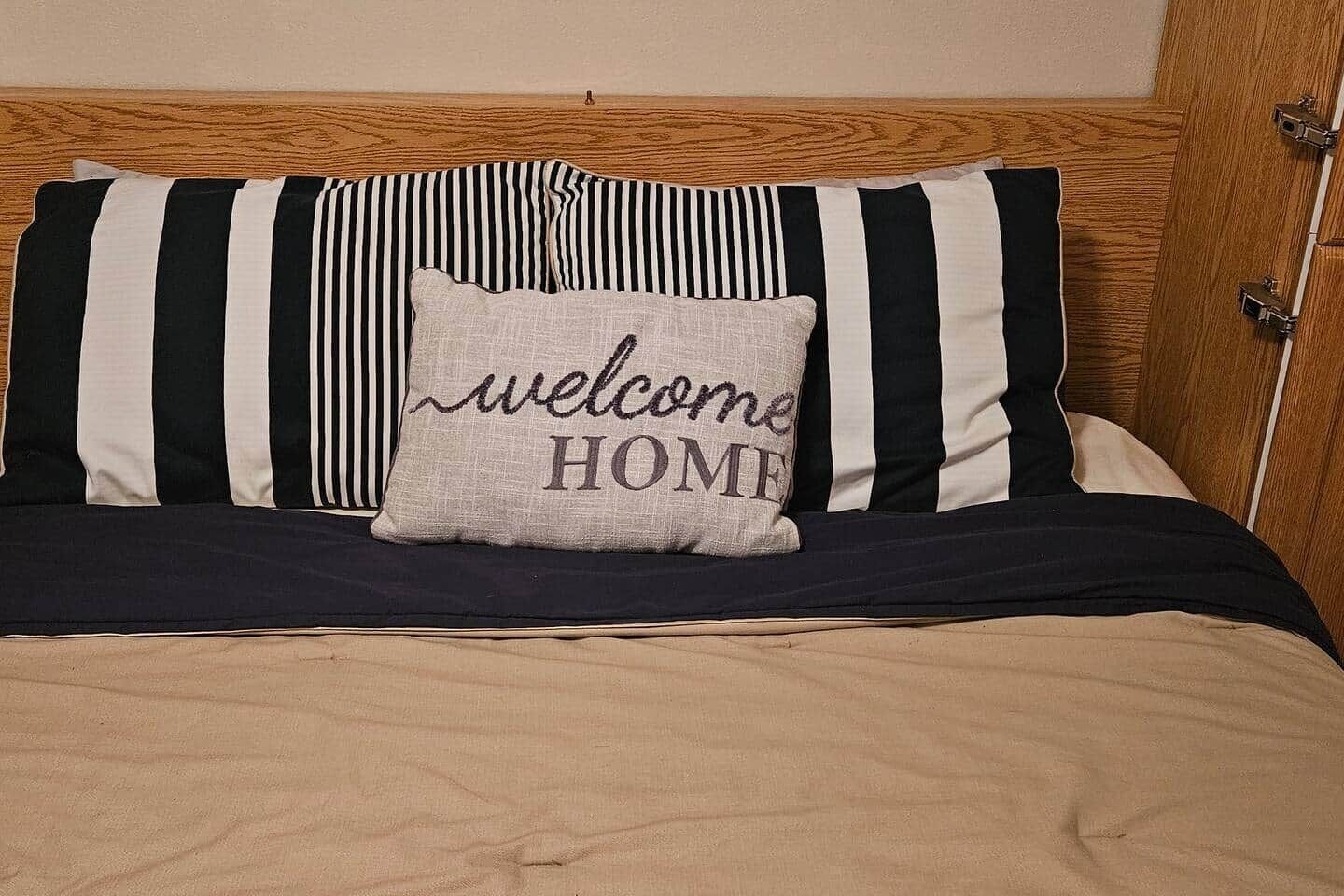 Een bed met streepjesbeddengoed en een kussen met de tekst 'welcome HOME'.