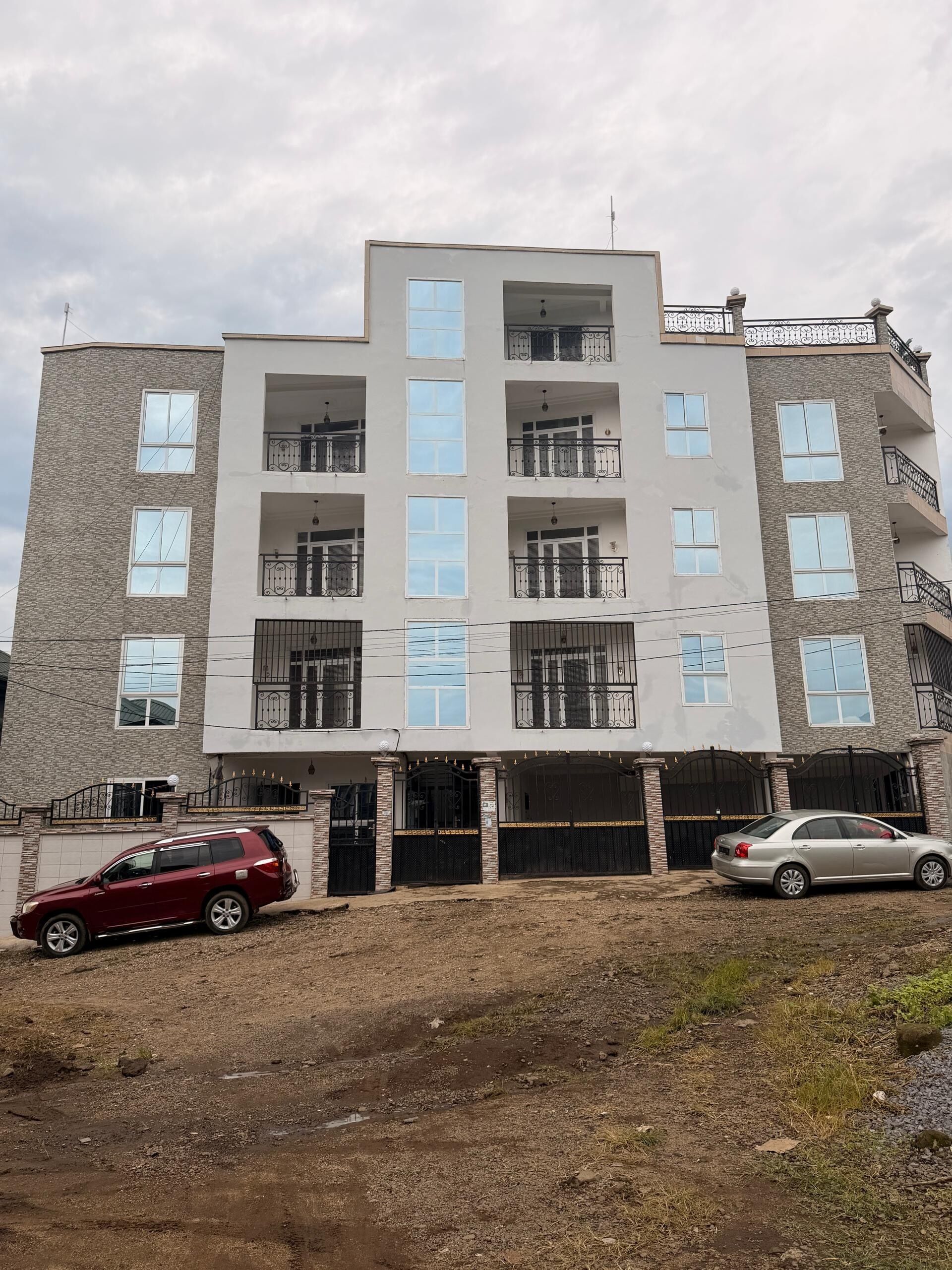 A multi-story residential building with a central entrance, balconies, and a gated driveway.