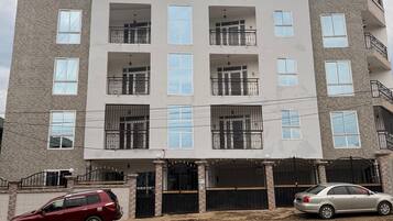 A multi-story residential building with a central entrance, balconies, and a gated driveway.