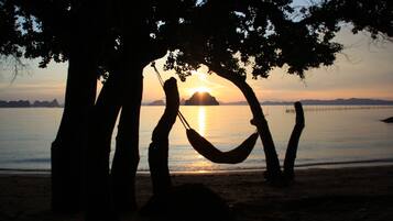 A hammock between trees on a beach with a sunset in the background.