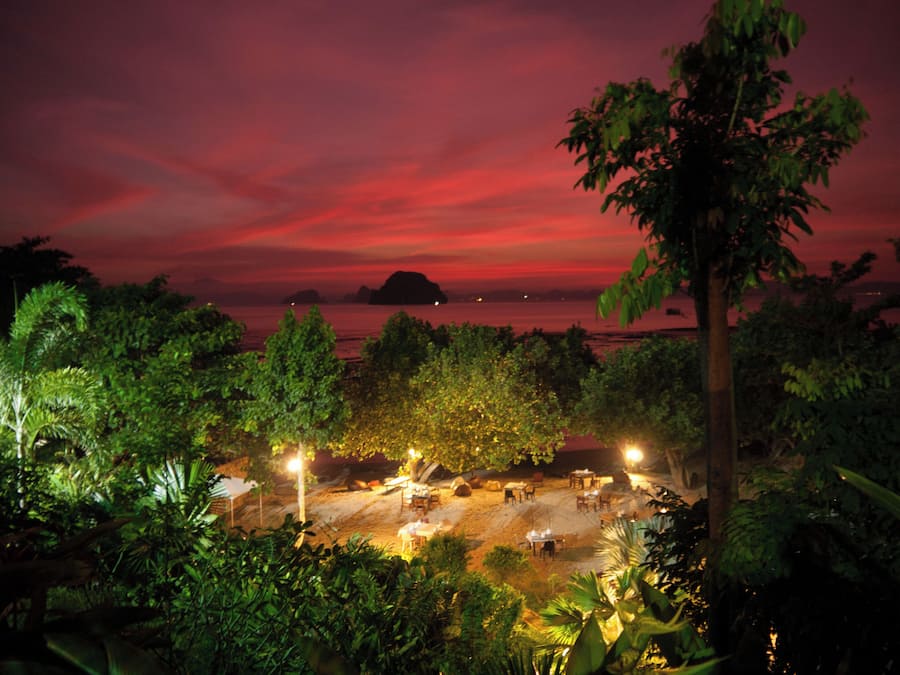 A beachside restaurant with outdoor seating, overlooking the sea and a sunset.