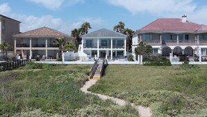 A beachfront property with a central building, a covered walkway, and surrounding greenery. - Luxury Beachfront Home w/ private beach access & private heated pool! (South Padre Island)