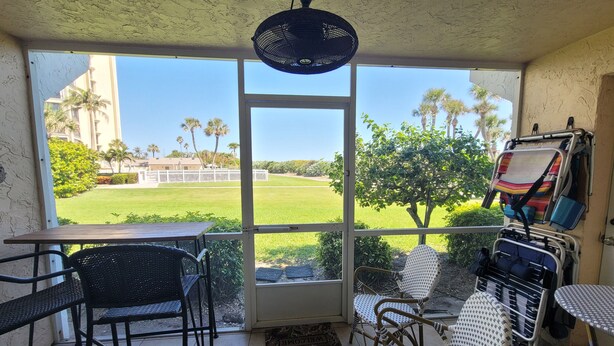 A room with a large window, wicker chairs, a table, and a ceiling fan. - CP 413 Dune View Condo - Welcome To Paradise! (Fort Pierce)