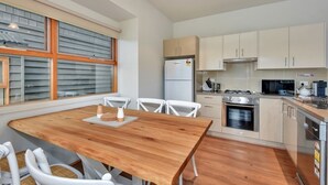 A modern kitchen with white cabinets, a wooden dining table, and a built-in oven. - The Chalet (Dinner Plain)