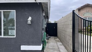 A narrow pathway leading to a dark-colored building with a tiled roof, a white-framed window, and a small white lantern on the wall. - New ADU -  Charming 1-bedroom house with AC, WiFi in fabulous Bakersfield (Bakersfield)