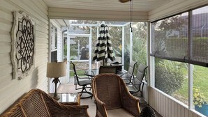Een overdekte veranda met rieten meubilair, een plafondventilator en uitzicht op de omgeving.