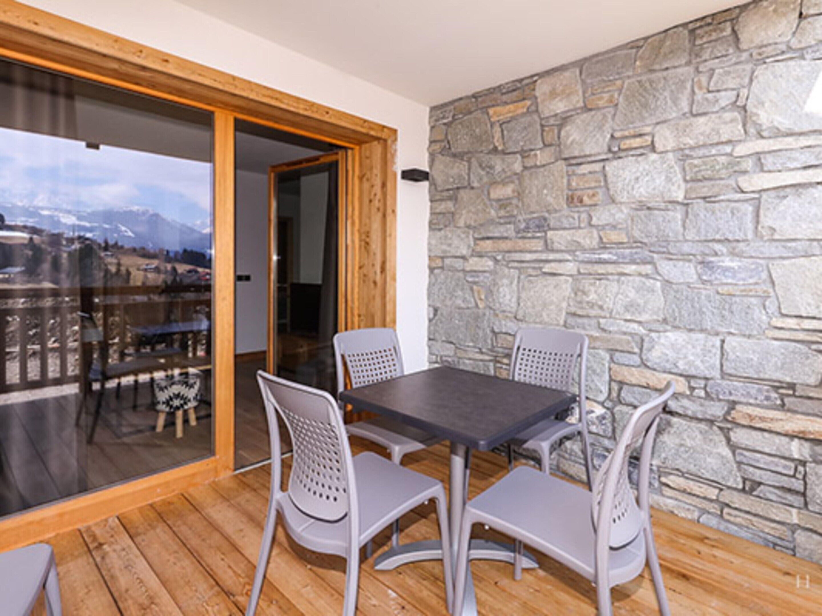 A balcony with a stone wall, a wooden floor, and a table with four chairs.