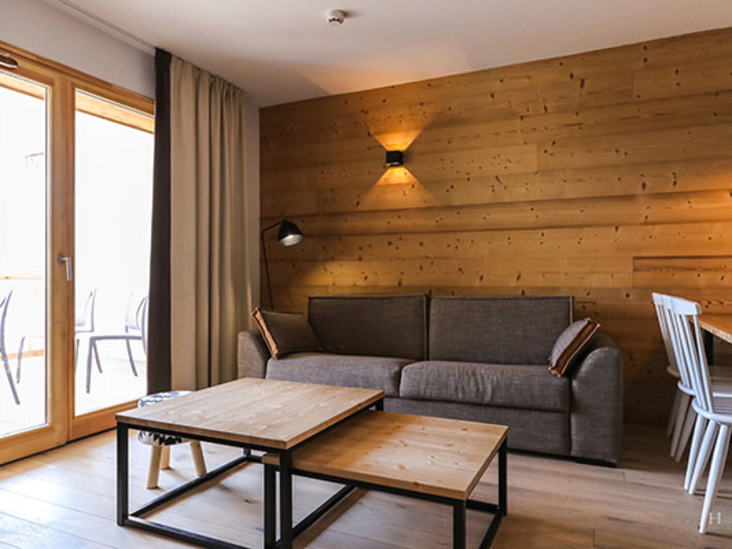 Een moderne woonkamer met een houten wand, een bank, een salontafel en een eethoek met stoelen.