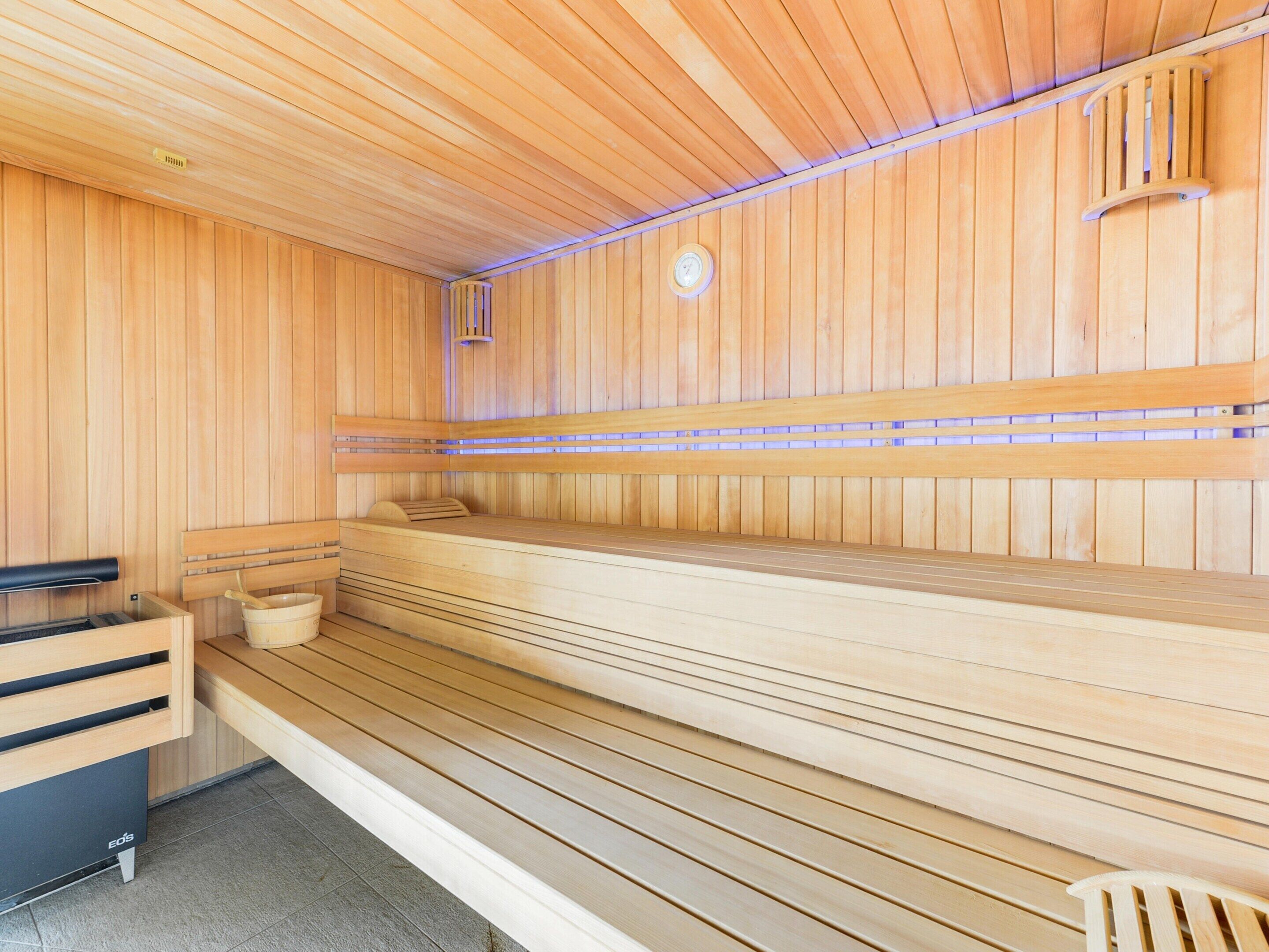 Un sauna avec des bancs en bois et un banc, une horloge et un radiateur au plafond.