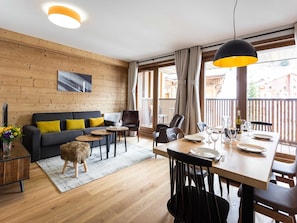 A modern living room with a sofa, coffee table, and dining area. - Apartment in Plagne 1800 Near Paradiski (La Plagne-Tarentaise)