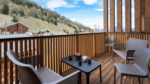 A wooden deck with a table and chairs, overlooking a mountainous landscape with buildings. - Apartment in Plagne 1800 Near Paradiski (La Plagne-Tarentaise)